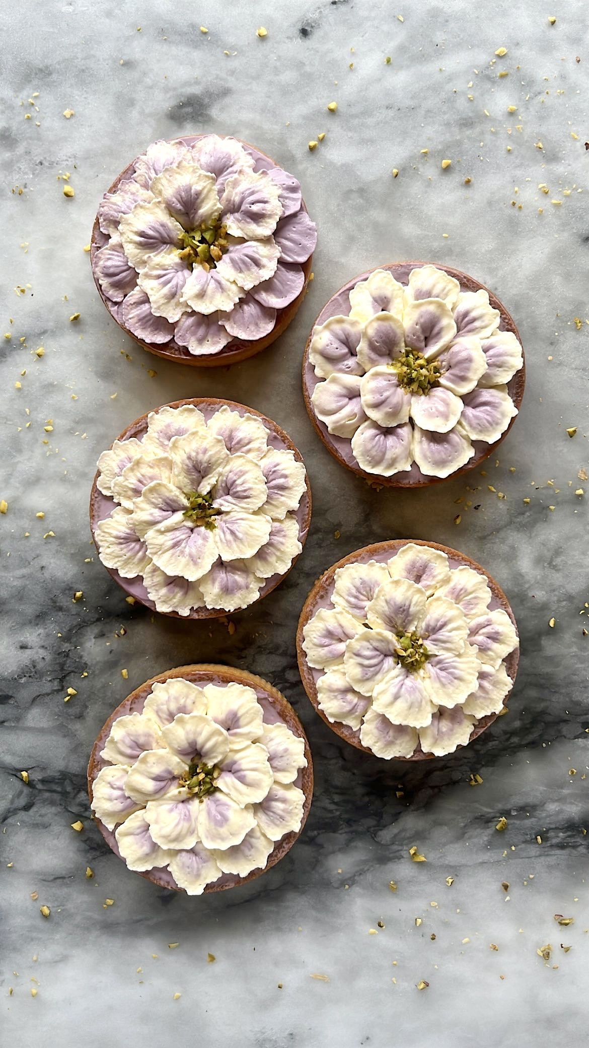 Five tarts decorated with purple and white flower-shaped cream piping on top